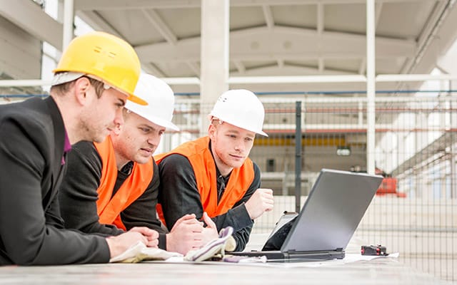 three men in hard hats looking at a laptop