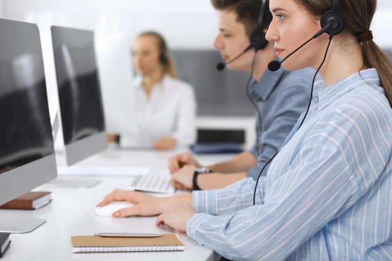 three people wearing headsets sitting in front of computers